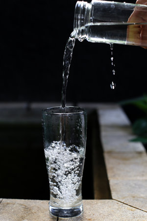 Pouring water into a glass on a wooden table in the gardenの写真素材
