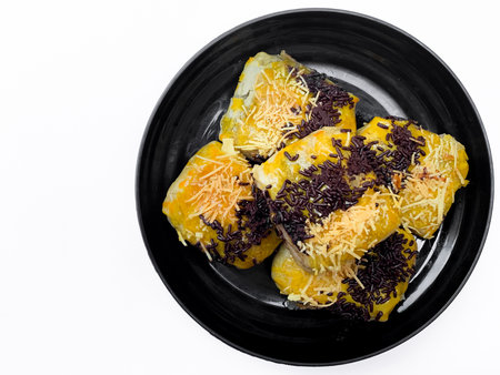 Close-up Indonesian chocolate banana bolen cake,indonesian banana puff pastry, garnished with grated cheese and chocolate. on a black plate isolated on white backgroundの写真素材