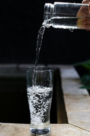 Pouring water into a glass on a wooden table, black backgroundの写真素材