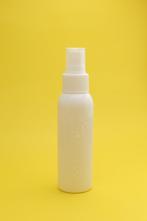 Isolated White Spray Bottle Against a Bright Yellow Background with Water Droplets.の写真素材
