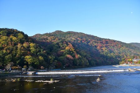 A view of the river and the autumn colours of the surrounding mountains, seen from Togetsu-kyo bridge.    Arashiyama Kyoto Japanの写真素材
