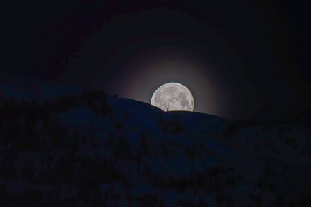 A picture of the moon peeking out from behind some mountains.   Whistler BC Canadaの写真素材