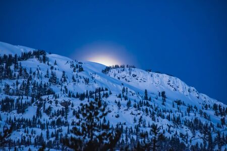 A picture of the moon peeking out from behind some mountains.   Whistler BC Canadaの写真素材