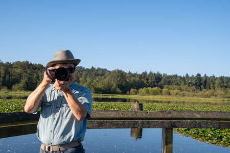 A picture of an Asian man wearing a hat and sunglasses who is taking pictures of a lake.   Vancouver BC Canadaの写真素材