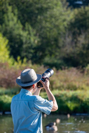 A picture of an Asian man with a hat and sunglasses aiming his camera upwards towards the sky.  ...
