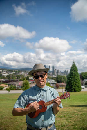 An Asian man at a park playing the ukulele while standing.   Vancouver BC Canadaの写真素材