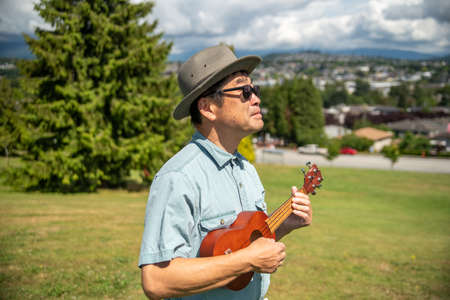 An Asian man at a park playing the ukulele while standing.   Vancouver BC Canadaの写真素材