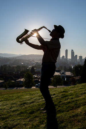 A silhouette of a man playing the alto saxophone on a hill as the sun rises.   Vancouver BC Canadaの写真素材