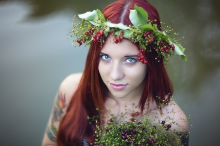 Bright girl with red hair. With a bouquet of berries and leaves on his head. The girl with a tattoo nature.の写真素材