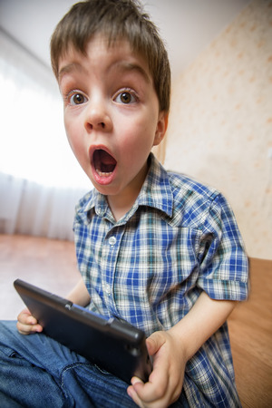 The boy with the tablet was very surprised at what he saw. Strong surprise. Optical distortion of the picture.の写真素材