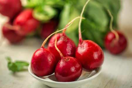 Red radishes in bowl on wooden table. Vegetable of cabbage family.の写真素材