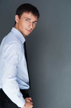 Closeup of a young smiling business man standing confidently against gray backgroundの写真素材