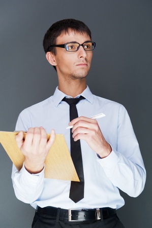 Closeup of a young smiling business man standing confidently against gray background and holding documents and map-caseの写真素材