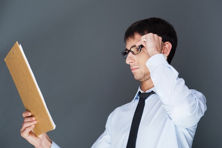 Closeup of a young smiling business man standing confidently against gray background and holding documents and map-caseの写真素材
