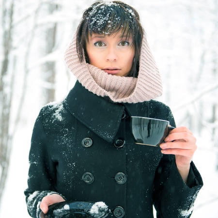 Portrait of young beautiful woman standing alone in winter park and drinking coffee. Take-away...