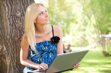 Portrait of a pretty student woman leaning on the tree trunk on foreground at summer parkの写真素材