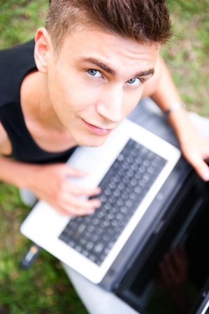 Closeup portrait of young student man using laptop and 3g usb modem for fast internet connection sitting outdoor at summer park on green grassの写真素材