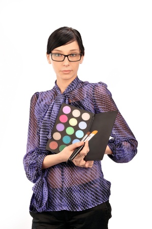 Closeup portrait of young woman professional visagiste holding brushes and eyeshadows in her arms wearing glasses and thinking about she`s new idea. Isolated on white backgroundの写真素材