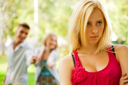 Upset teenage girl being jeered by group of the other young people gossiping in park の写真素材