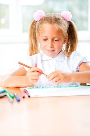 Little girl looking for a drawing concept wile painting picture on paper sheet. Indoors at classroom. Vertical Shotの写真素材