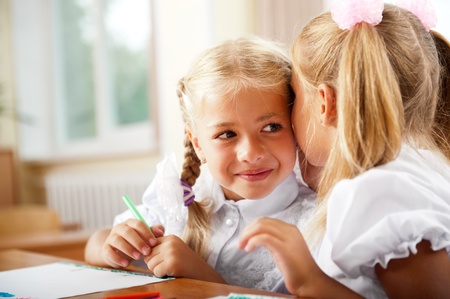 Two little girls gossip in classroomの写真素材