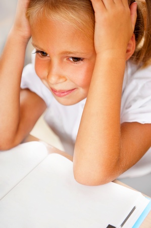 Image of smart child reading interesting book in classroom. Vertical Shot. She is tiredの写真素材