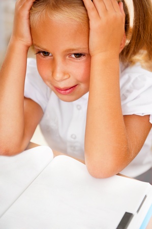Image of smart child reading interesting book in classroom. Vertical Shot. She is tiredの写真素材