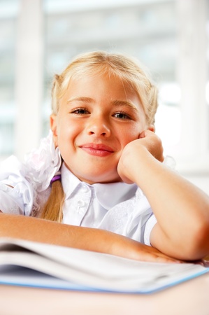 Portrait of a young girl in school at the desk  Vertical Shot  Looking at camera and holding chin by her armの写真素材