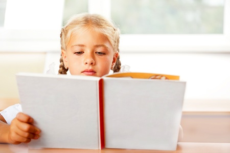 Image of smart child reading interesting book in classroom. Horizontal Shot. She is involved and thinkingの写真素材