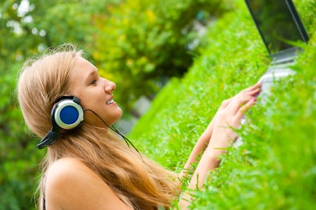 A smiling young girl with laptop outdoors listening music by headphonesの写真素材