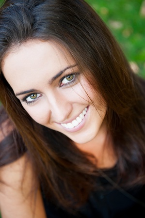 Portrait of smiling young girl sitting on grass in the forest and looking at youの写真素材