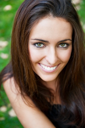 Portrait of smiling young girl sitting on grass in the forest and looking at youの写真素材