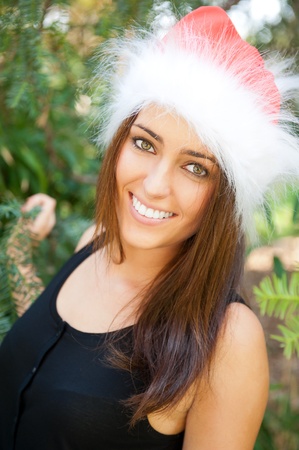 Portrait of a sexy young female smiling in a park and looking at camera wearing elegant dress and christmas Santa Claus hat. Happy New Year on vacation at Warm Countryの写真素材