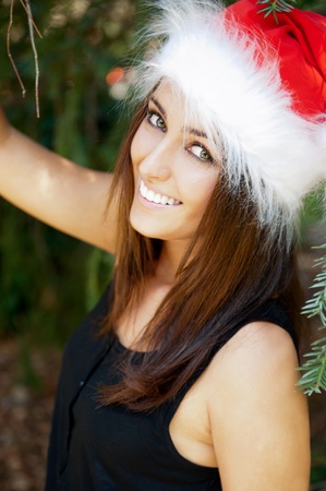 Portrait of a sexy young female smiling in a park and looking at camera wearing elegant dress and christmas Santa Claus hat. Happy New Year on vacation at Warm Countryの写真素材