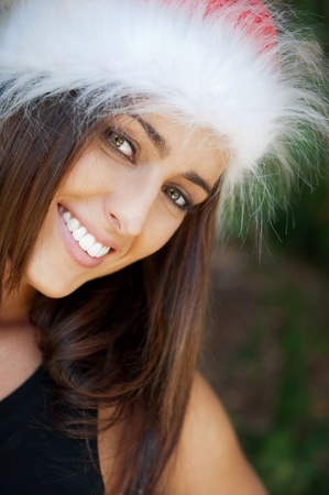 Portrait of a sexy young female smiling in a park and looking at camera wearing elegant dress and christmas Santa Claus hat. Happy New Year on vacation at Warm Countryの写真素材