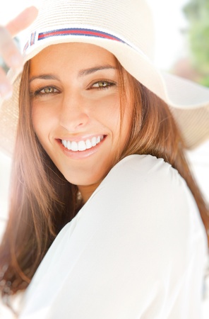Portrait of pretty cheerful woman wearing white dress and straw hat in sunny warm weather day. Walking at summer park and smiling の写真素材