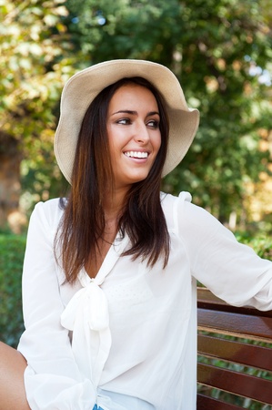 Portrait of a sexy young female smiling in a park while sitting on bench and looking away - Outdoorの写真素材