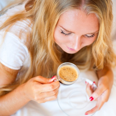 Smiling woman drinking a coffee lying on a sofa at homeの写真素材