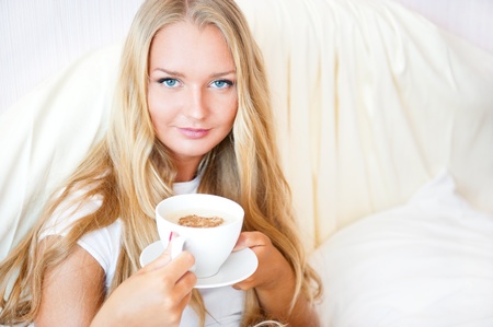 Smiling woman drinking a coffee lying on a bed at home or hotel.の写真素材