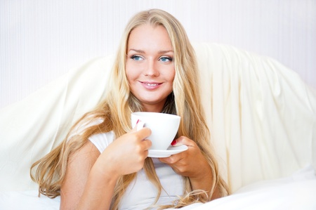 Smiling woman drinking a coffee lying on a bed at home or hotel.の写真素材
