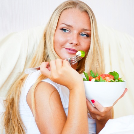 Closeup portrait of a beautiful slender girl eating healthy food  at bed. She is on vacation.の写真素材