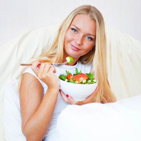 Closeup portrait of a beautiful slender girl eating healthy food  at bed. She is on vacation.の写真素材