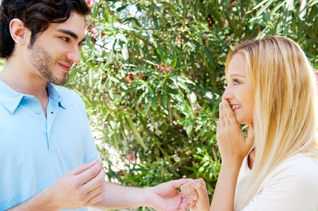 Happy young hispanic man gifting a ring to a beautiful surprised young caucasian woman in a parkの写真素材