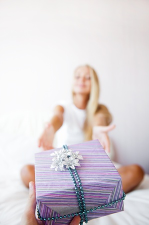 Boyfriend making a gift to his girlfriend in the morning. She is sitting on bed and taking gift box. Smiling laughing and very happyの写真素材