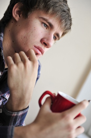 Happy young handsome man at home, drinking coffee or tea near windowの写真素材