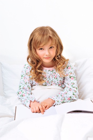 Closeup portrait of adorable little girl resting in her bed with white with beautiful long curly hairの写真素材
