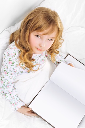 Closeup portrait of adorable little girl resting in her bed with white with beautiful long curly hairの写真素材