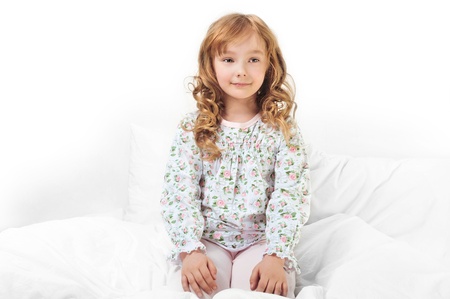 Closeup portrait of adorable little girl with beautiful long curly hair resting in her bed with white linenの写真素材
