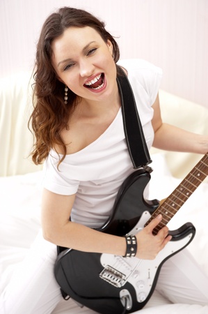 Portrait of young pretty girl who is feeling free and playing guitar in a roomの写真素材