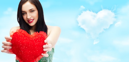 Cute young woman holds a heart symbol against romantic background with lots of copyspaceの写真素材
